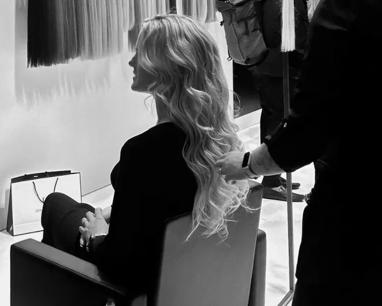 Friseurschulung zur Extensionsanbringung – Stylist stylt lange gewellte Haarverlängerungen an Modell im Salon